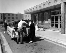 Students load suitcases into the trunk of a car in front of Mitchell Hall (1958), St. Cloud State University