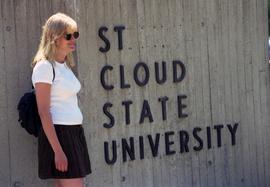 A woman stands in a front of a sign, St. Cloud State University