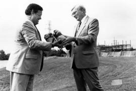 Robert Bess and St. Cloud mayor Chuck Winkelman exchange symbolic parcels of direct to signify the official exchange of property along the Mississippi River, St. Cloud State University