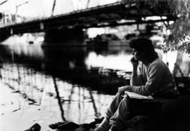 Student Holly George sits near the University Drive bridge and the Mississippi River