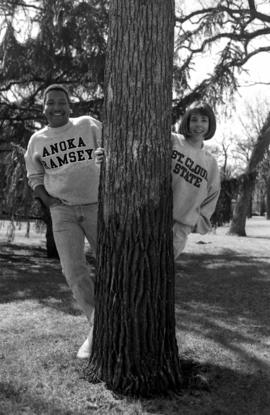 Sara Grachek and another student peek around a tree, St. Cloud State University