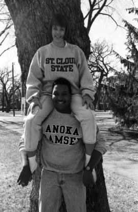 Two students lean against a tree, St. Cloud State University