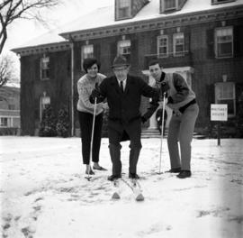 Dale Patton stands on a pair of skis with students David Weber and Mary Piram in front of Whitney House (1956), St. Cloud State University