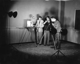 Three men set up a movie camera and projector, St. Cloud State University