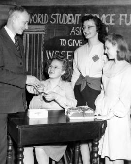 Dudley Brainard purchases a World Student Service Fund ticket from Winnifred Hansen, Mary Louis Mayberry, and Mavis Kennedy, St. Cloud State University