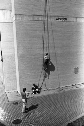 Al Cottingham climbs an Atwood Memorial Center (1966) wall while Joel Lindmeer and Joel Dhien look on, St. Cloud State University