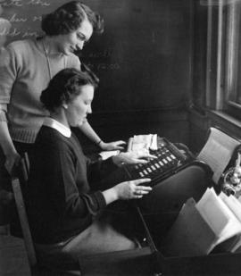 Lucile Pearson (standing), Eleanor Niemi (seated) learn how to use an adding machine, St. Cloud State University